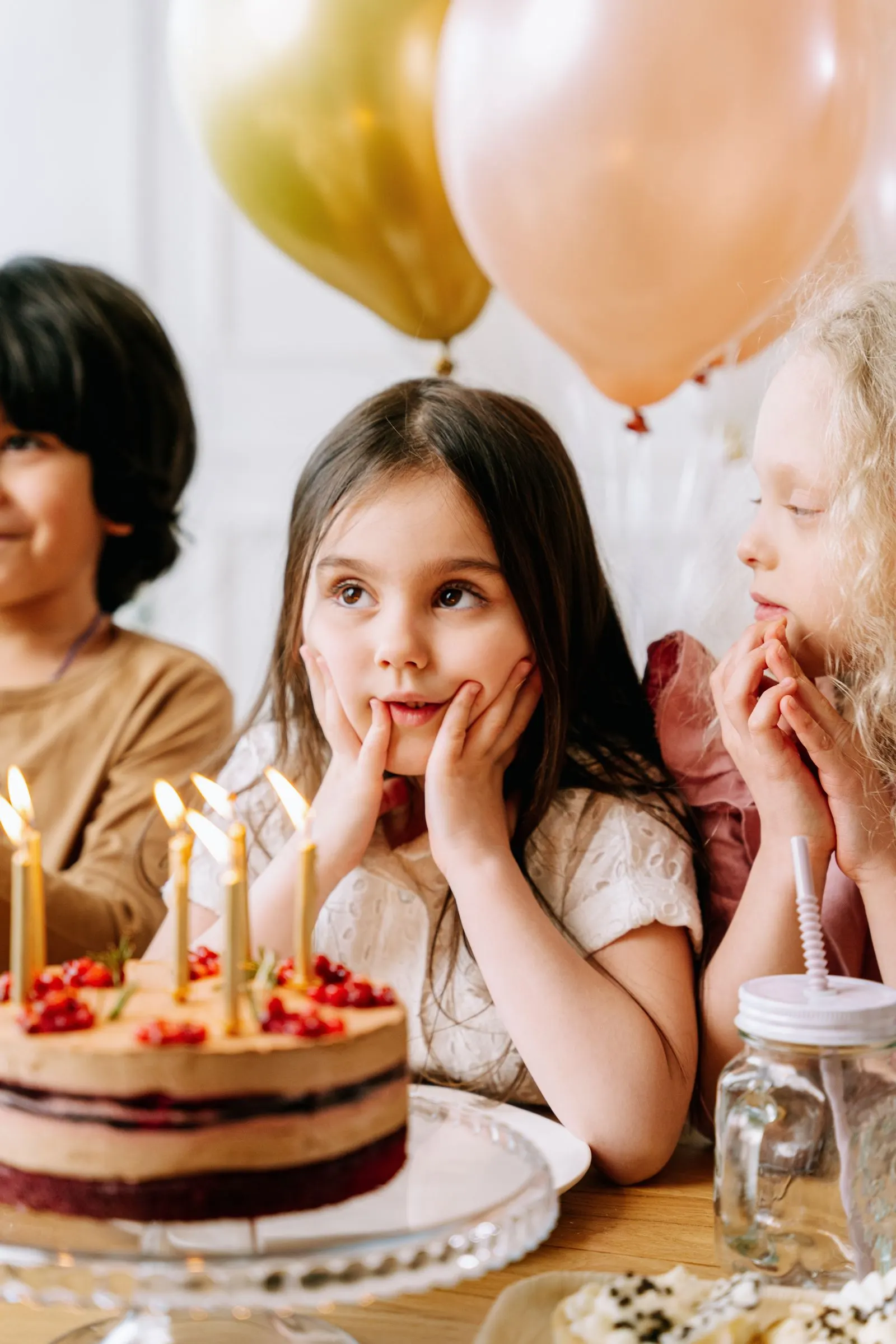 Barn feirer bursdag rundt et bord med kake og ballonger